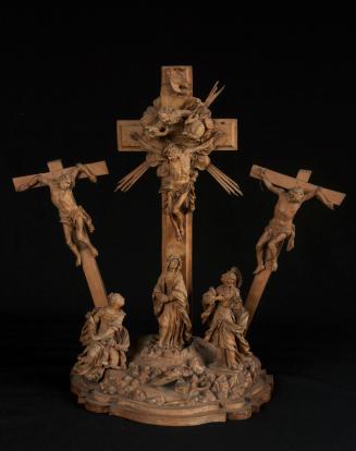 The image shows a sculptural representation depicting a crucifixion scene. In the center, there is a tall crucifix with a figure nailed to the cross. On both sides of the central cross, there are additional figures also hanging from crosses. Beneath the crucifix, a group of figures is arranged, including a central figure that represents a female figure, with two more figures standing on either side. The entire composition is richly decorated and conveys a religious theme.

[AI-generated with C…